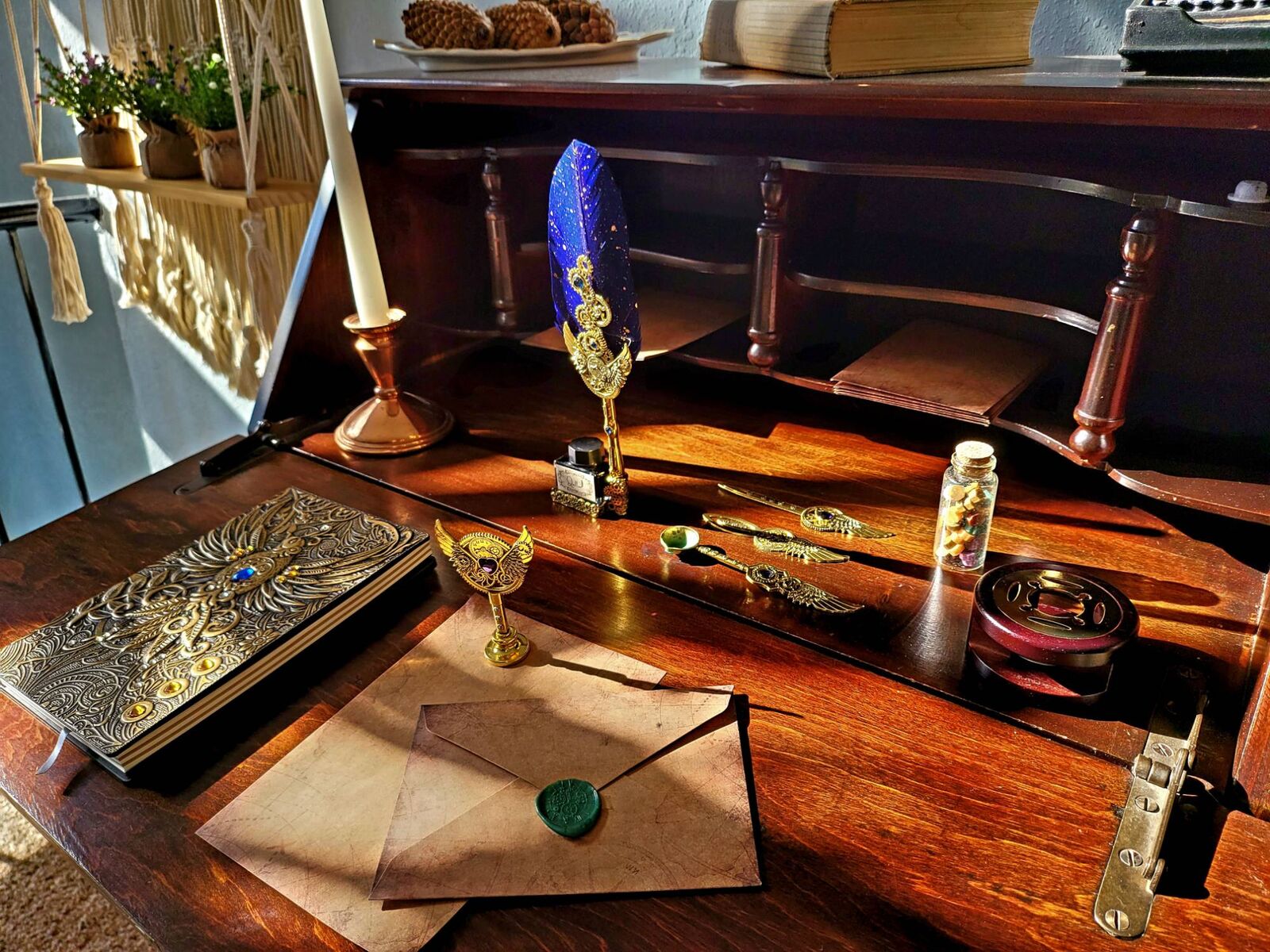 An old secretary desk open in late sun: a blue quill in a gilded stand beside a bottle of ink, a letter sealed with green wax, a jewelled journal and a jar of sealing-wax beads.