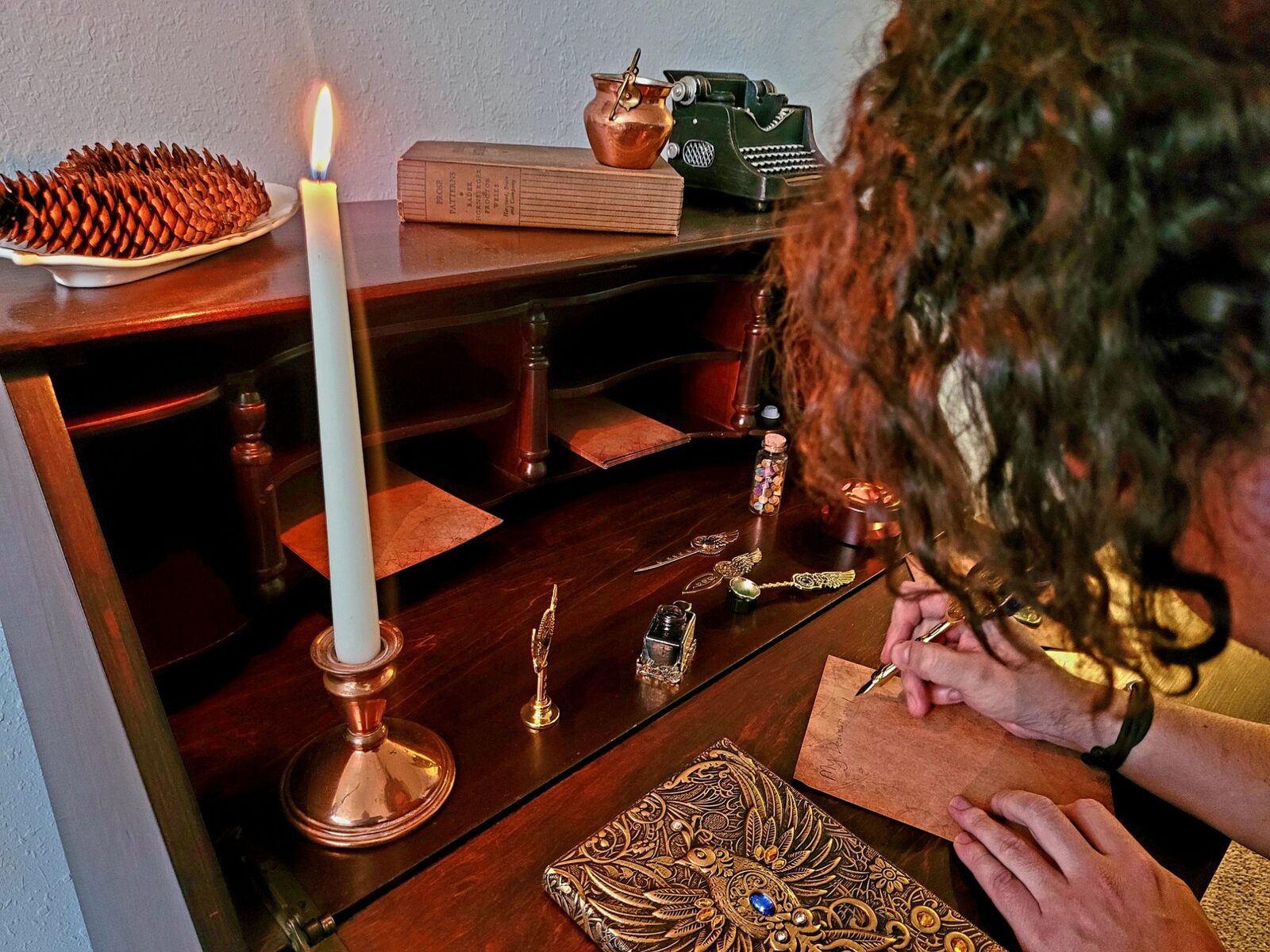 A guest writing a letter with a dip pen at the secretary desk by candlelight, the ink, the wax spoon and the seals set out beside the page.