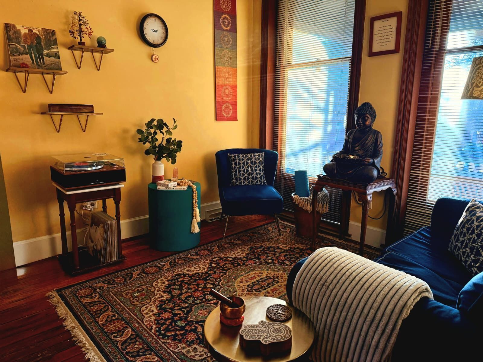 A record player beside a blue velvet chair and a deep blue sofa, an antique rug across the floor in morning light.