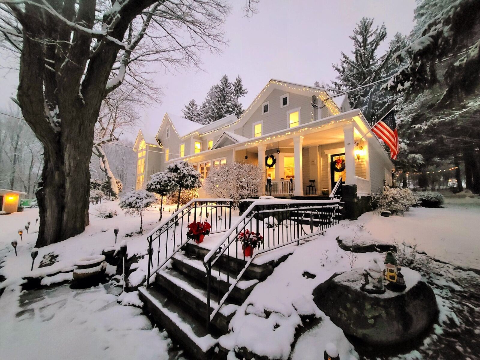 The Pump House at dusk after a snowfall, its porch and windows lit at the top of the stone steps.
