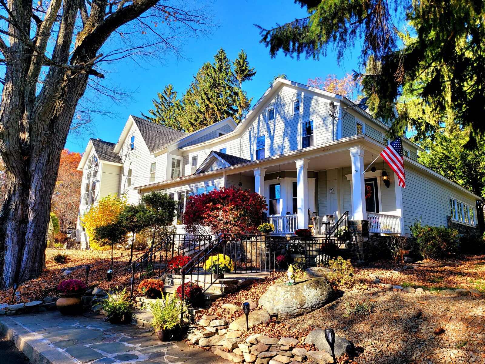 The Pump House in autumn sun, a large white historic house with a long porch, red leaves along its stone steps.