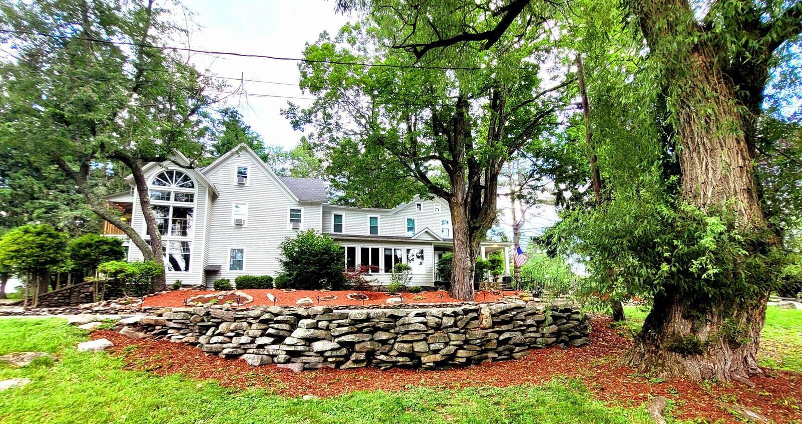 The Pump House seen across the lawn, a white historic house behind old trees and a ring of fieldstone.