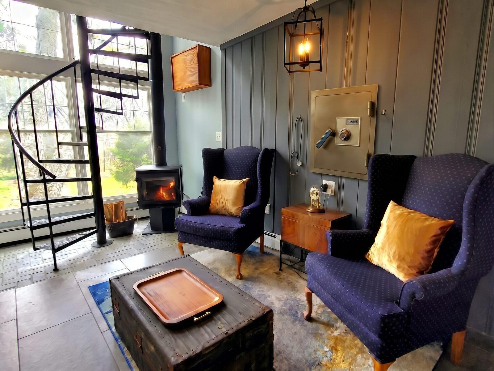 Two blue wingback chairs by the old safe and the stethoscope, a wood stove and a spiral stair by the windows.