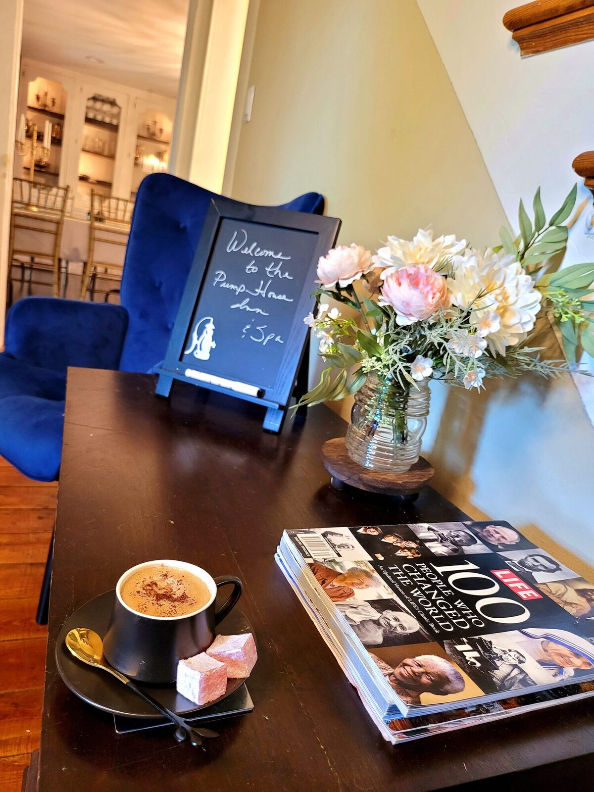 A handwritten welcome note on a small easel by a vase of roses, coffee and a book set out beside it.