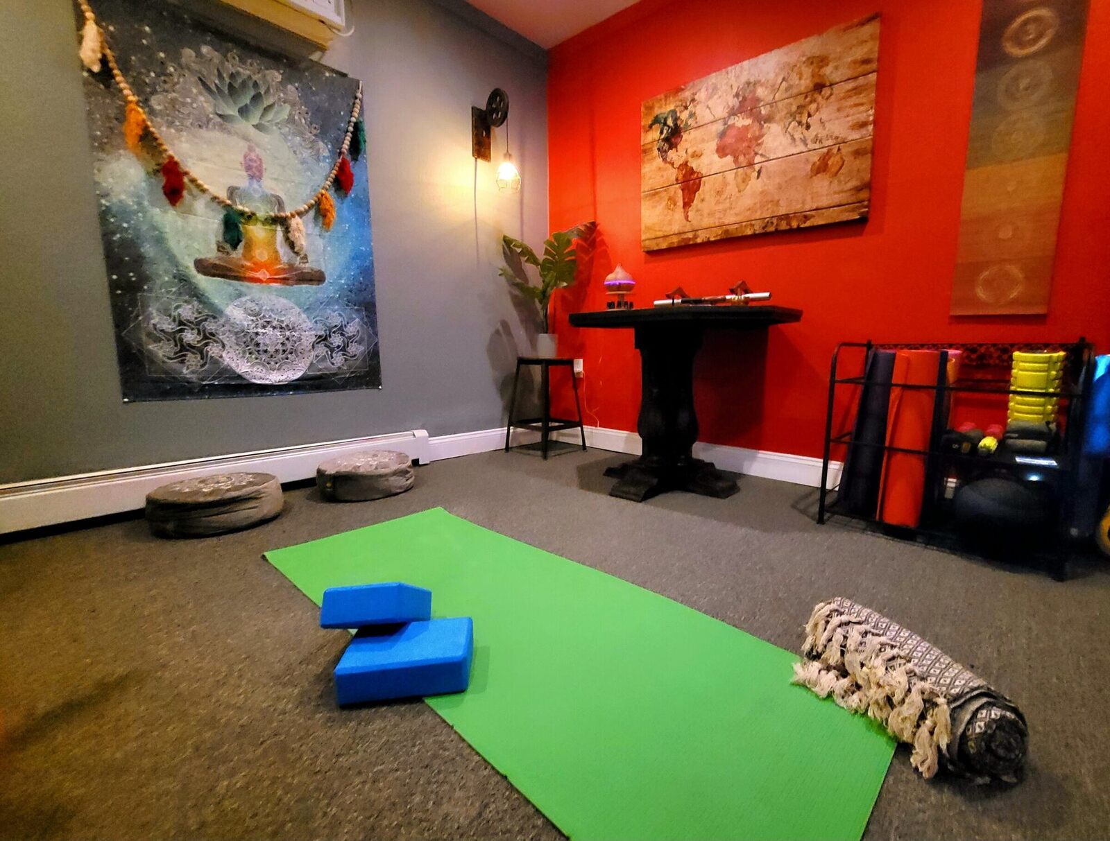 The Pump House yoga room, a green mat laid out with two blocks and a rolled blanket, a red wall and a tapestry behind.